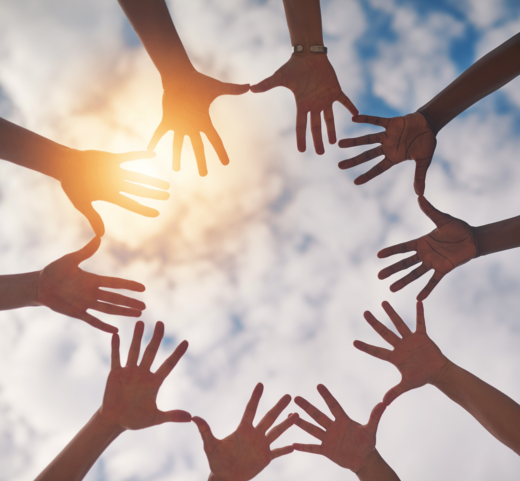 Connecting with nature and each other. Low angle shot of a group of unidentifiable people making a circle with their hands against a cloudy sky.